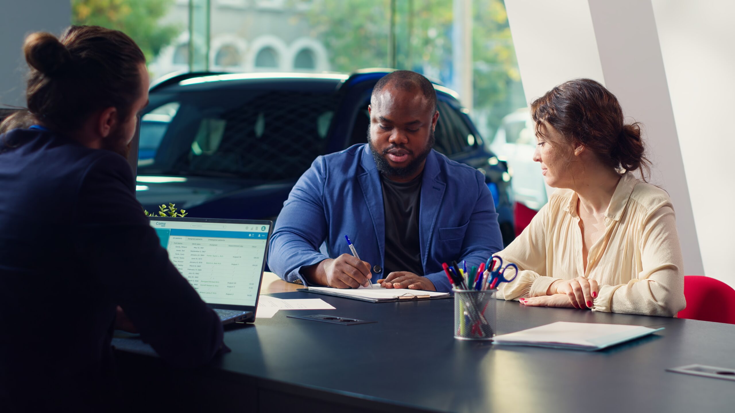 Car dealership salesman sitting with clients at table, giving them contract to sign