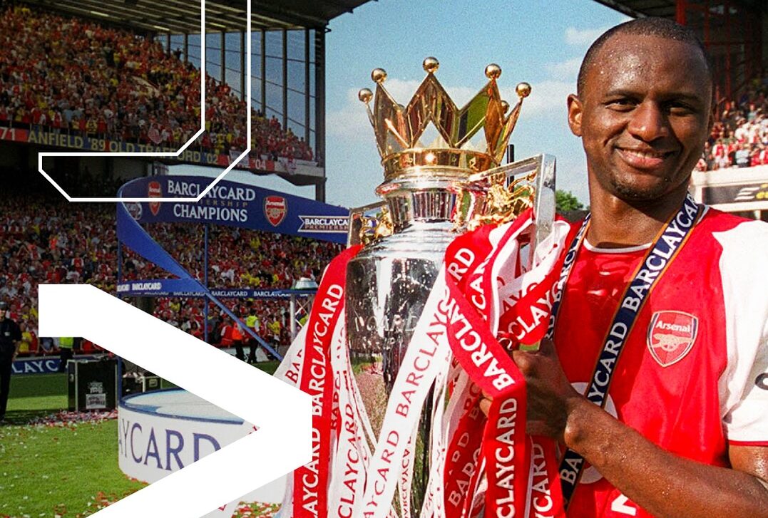 Patrick Vieira, the new Senegal head coach, standing confidently on a football pitch with Senegalese stadium in the background