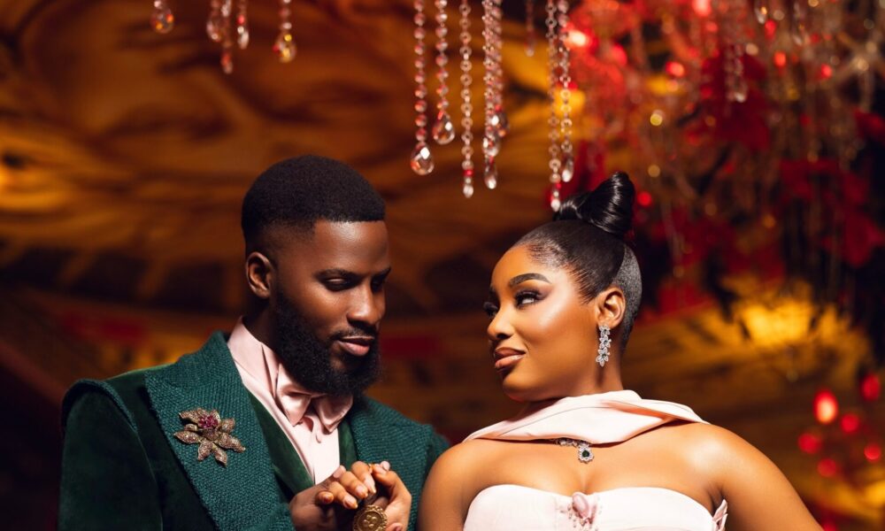 Akin Faminu and Kiky Festus in coordinated forest green and blush pink outfits, posing elegantly in a pre-wedding photoshoot setting with soft lighting and natural greenery.