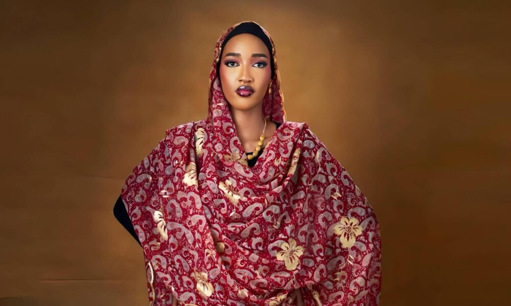 A young Nigerian creative in a stylish Ankara outfit, holding a professional camera in a modern urban setting with African decor.