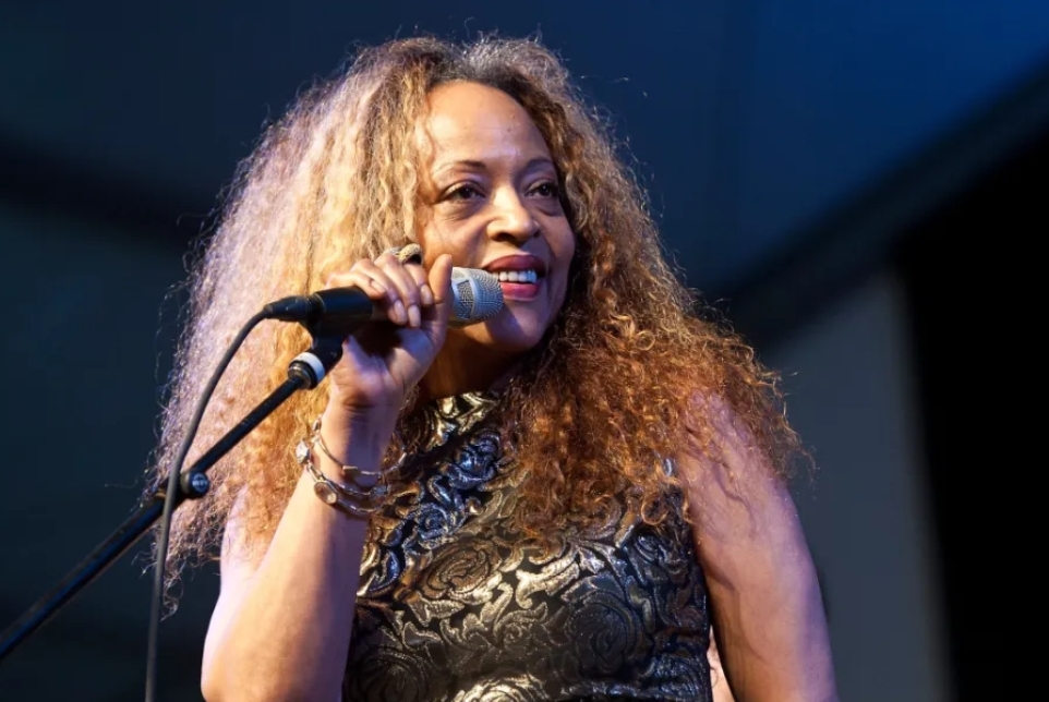 A glowing vinyl record on a wooden table with sheet music and a saxophone, set against African textile patterns, symbolizing Cassandra Wilson's jazz legacy.