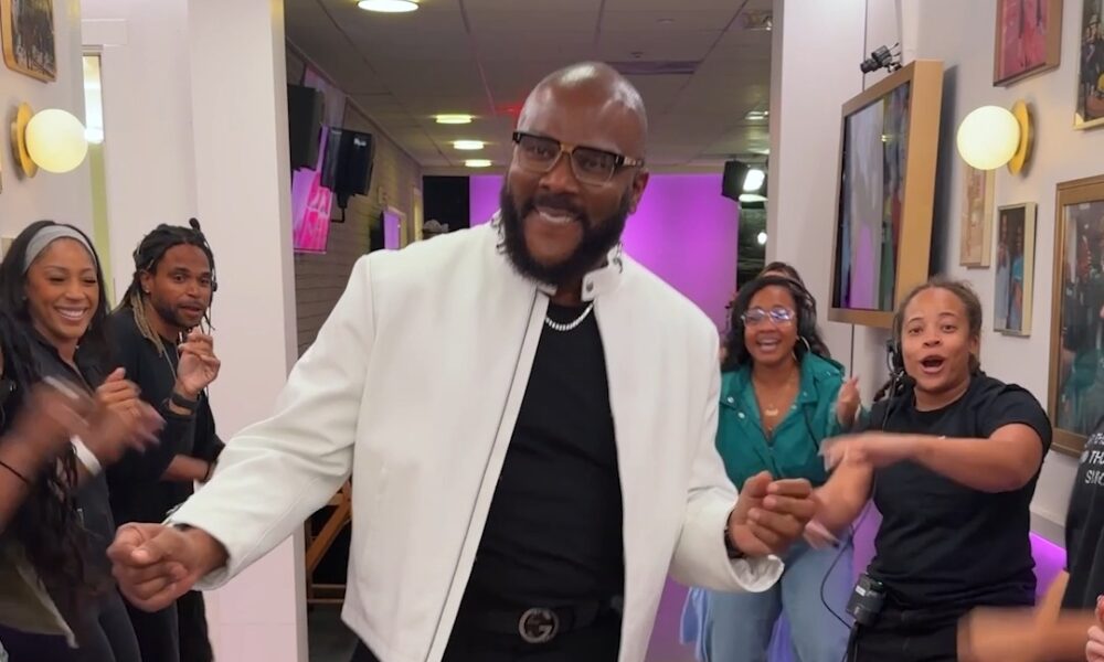 Stylish white leather jacket and Gucci belt in a TV studio corridor, hinting at Tyler Perry’s recent dance moment.