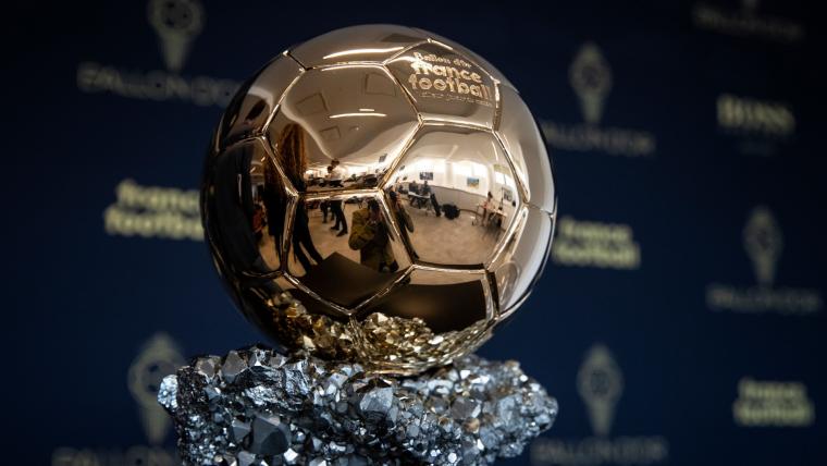 Golden Ballon d’Or trophy on African kente‑style fabric with stadium blur