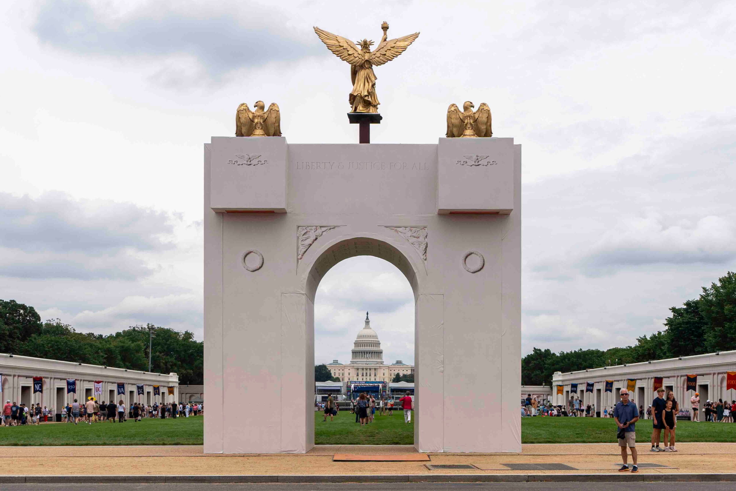 Unfinished marble arch on the National Mall under a sunrise, with security fences and drones overhead
