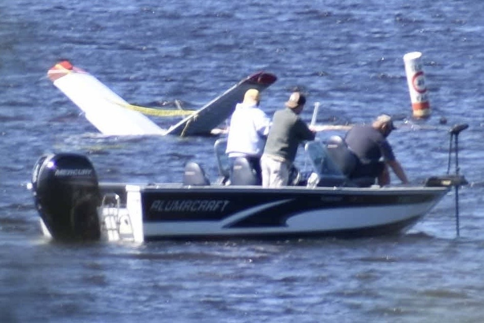 Small aircraft after emergency landing on a lake with rescue boats nearby