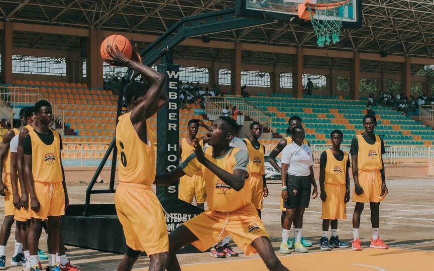 Young African basketball players practicing on an outdoor court in Lagos as the sun sets.