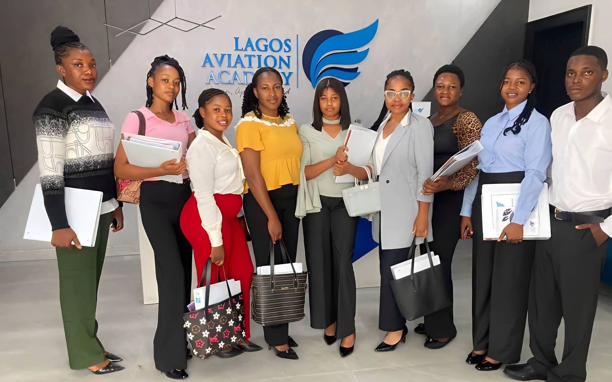 Nigerian youths in aviation academy classroom, seated in cabin crew uniforms, listening to an instructor.