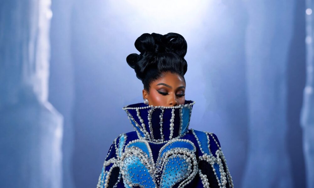 Ice blue velvet evening coat-gown with pearl and cobalt accessories displayed on a dark wooden hanger in a studio setting