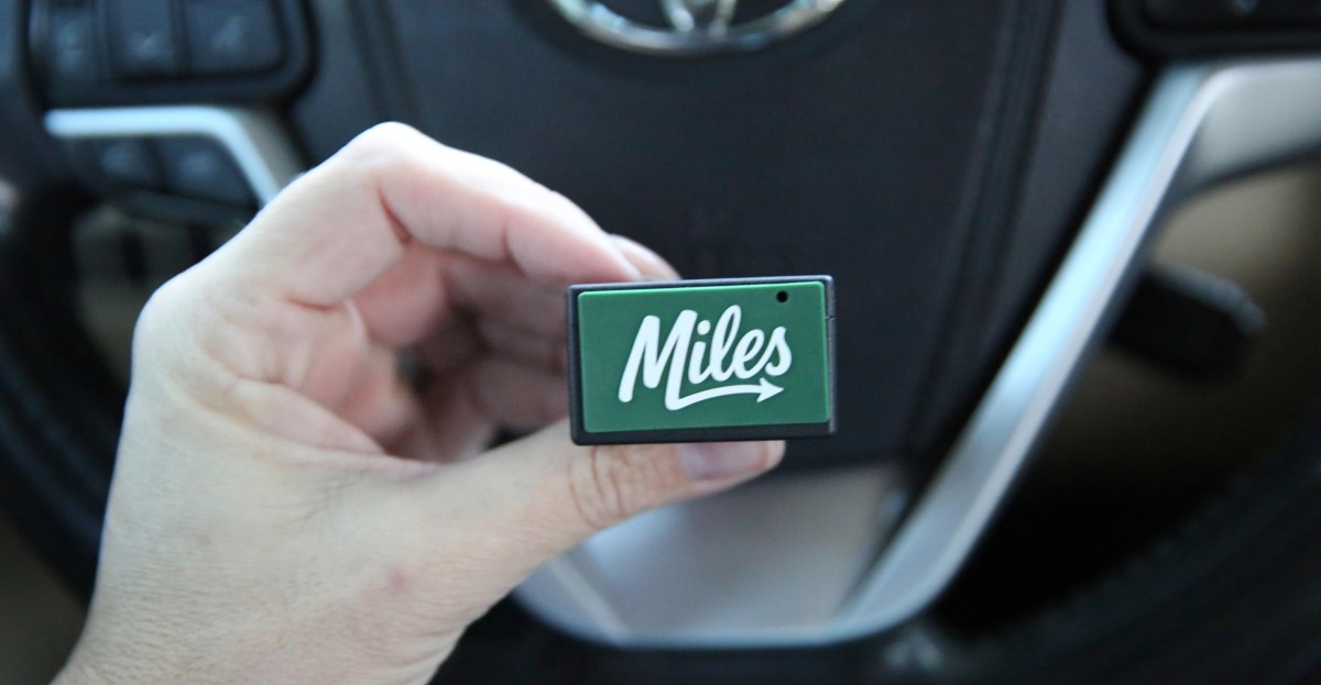 Black OBD‑II plug connected to a car’s diagnostic port, hinting at data tracking and safety features.