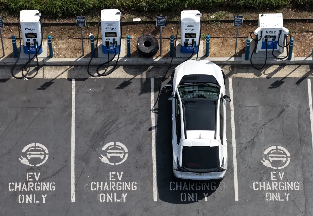 Electric vehicles and charging stations along a highway with solar panels on homes