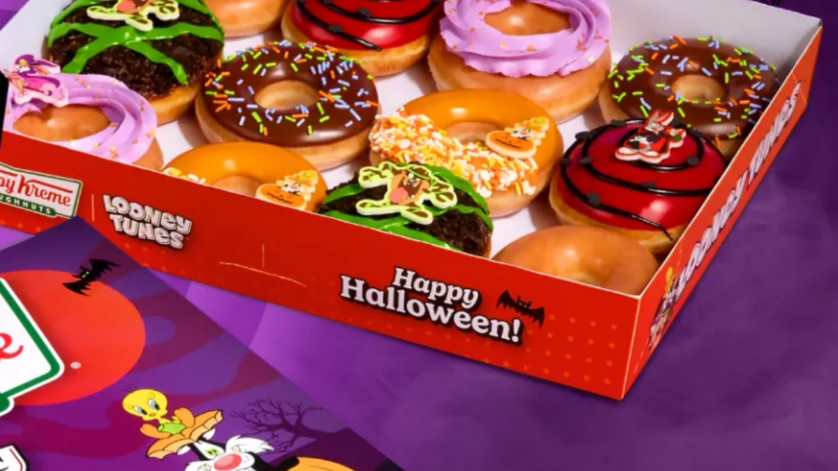 Three Krispy Kreme glazed doughnuts shaped like Looney Tunes characters displayed on a festive table with Halloween accents