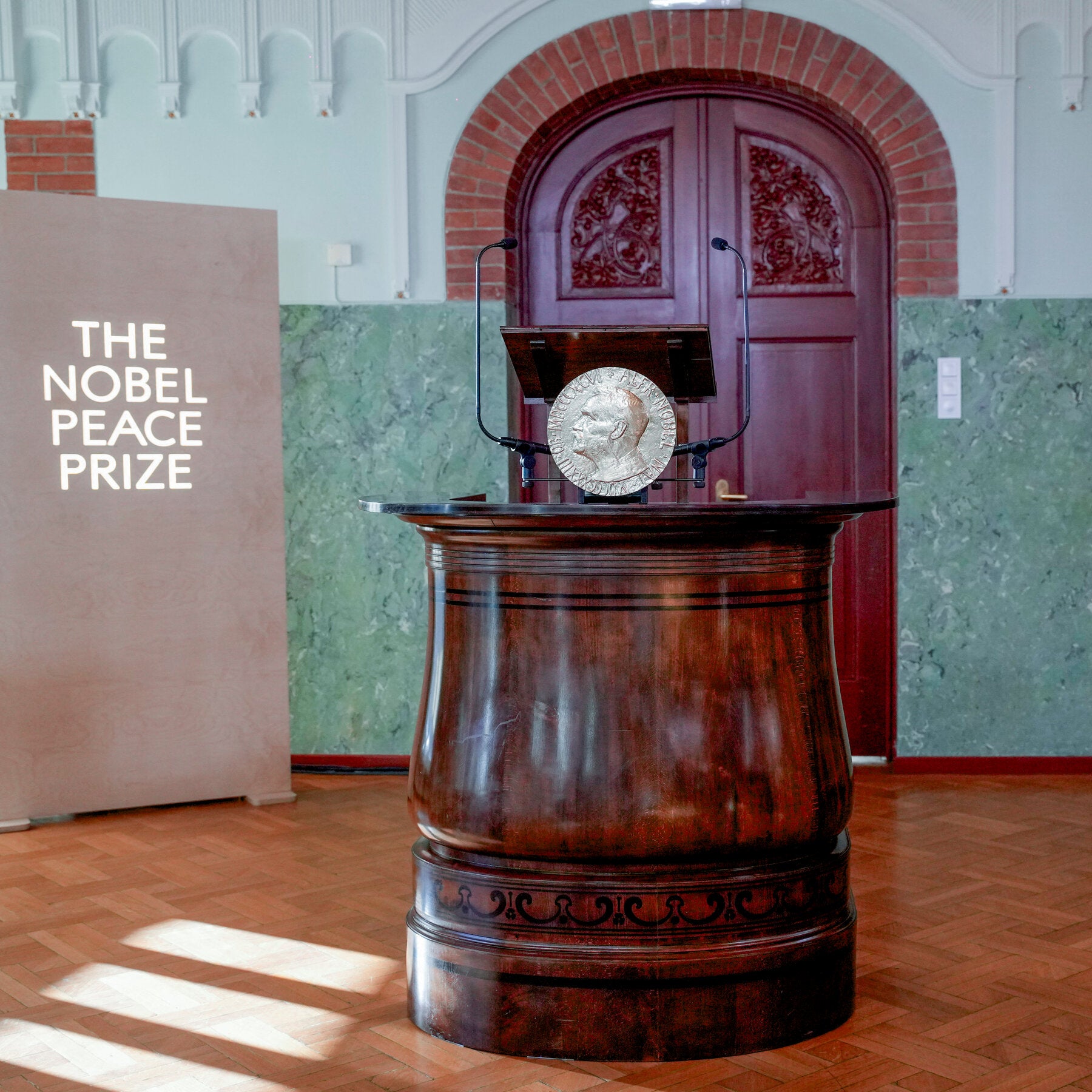 Symbolic Nobel medal above a live broadcast camera in a dim cityscape, representing the controversy.